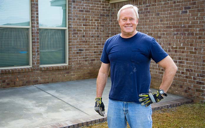 Danny Lipford, vestido con una camisa de manga corta, se para y sonríe frente a un patio de concreto recién terminado.