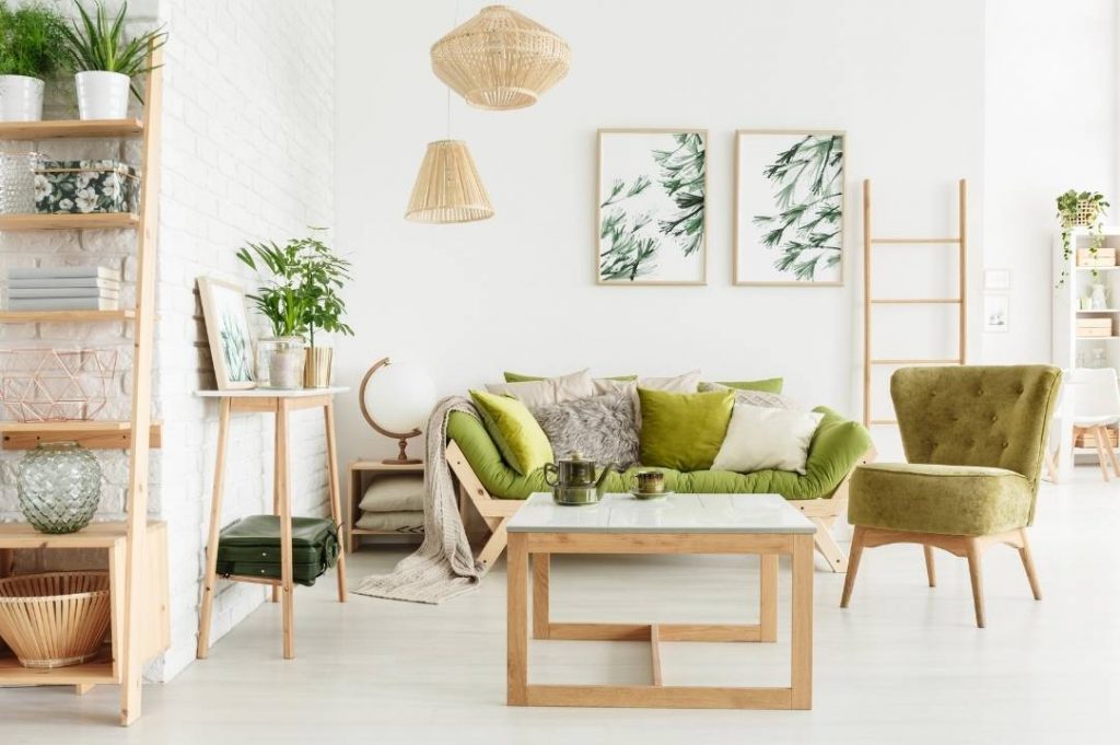 Sala de estar estilo jungla con sofá verde y sillón.  Librería con plantas y cuadros con plantas verdes.