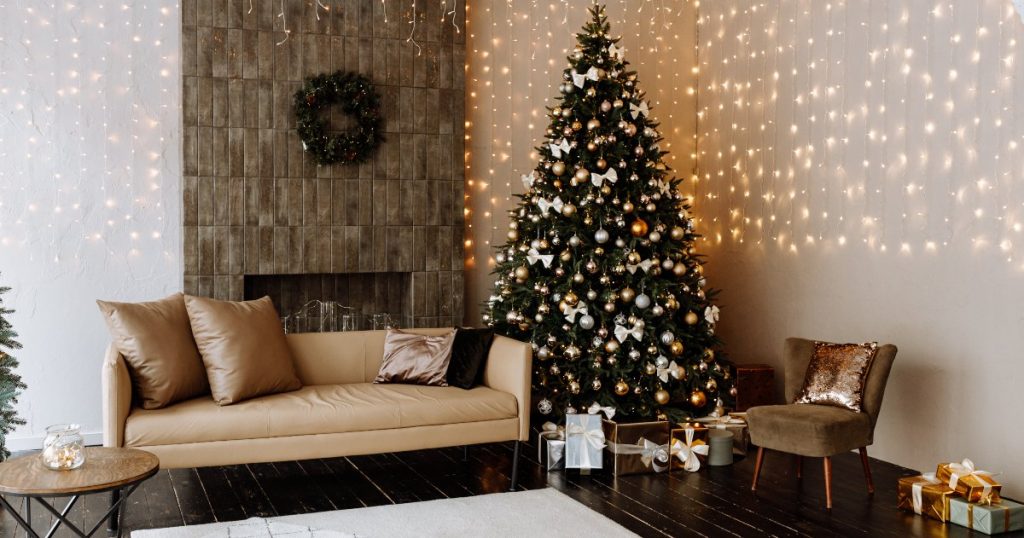 Salón con árbol de Navidad junto a un sofá beige y luces decorativas.